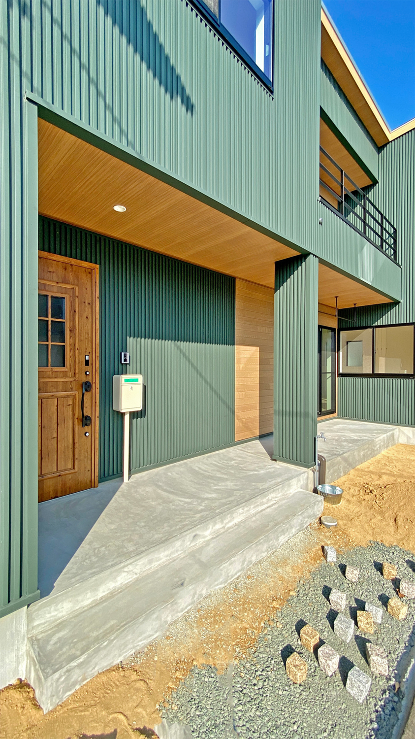 モスグリーン色のガルバリウム鋼板 木目調の玄関ドアで石目柄のsolidがひきたつ。株式会社藤工務店