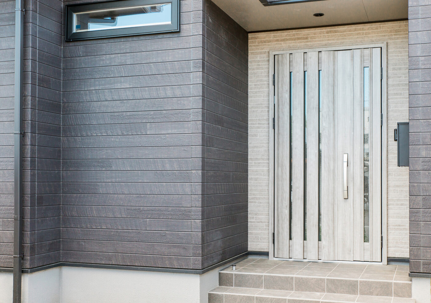 グレー×ブラック のバランスが良い外壁と木目調のドアが 魅力的な施工事例 シンプルなBOX型のプランにさりげない窓配置 ▽青空 ▽サイディング ▽木目調サイディング外観キッチンインテリア施工事例外壁グレー