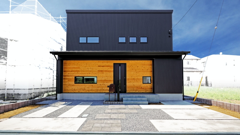 ブラックのガルバリウム鋼板と木目調のサイディングが美しく調和した、建築家らしい外観デザイン。変形地を活かした建物の配置、片流れの屋根、木の軒