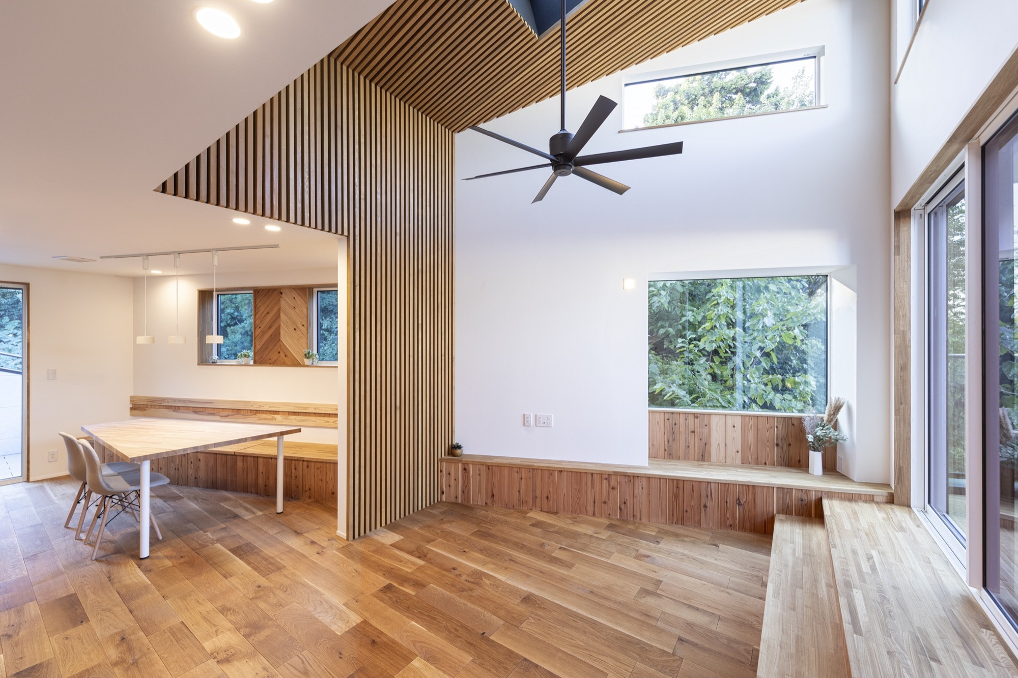 間接照明に照らされて、勾配天井の木目がゆたかな表情をもたらすダイニング。掃出窓を天井いっぱいの高さまで設けたことで、無駄なラインのない洗練さ